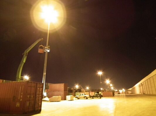 Night view of a UK container yard with high mast LED lighting and a lift truck working near the pole